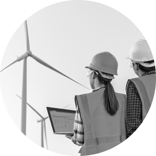 Woman and man in high visibility jackets and hard hats looking at wind turbines while viewing data on a laptop screen