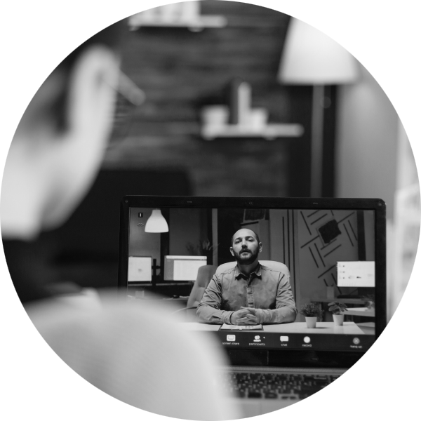 A woman watching a webinar with a seated man on her laptop screen talking to camera