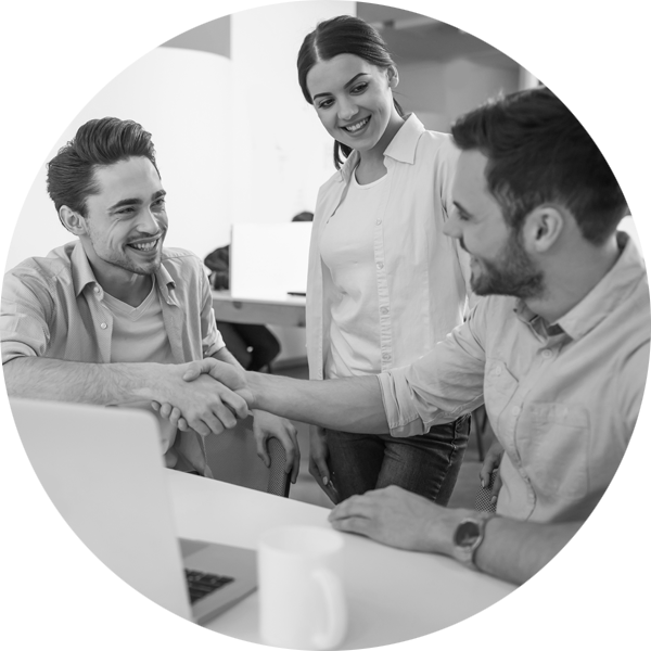 Businesspeople smiling and shaking hands while a happy colleague looks on